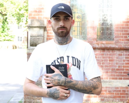Young man with tattoos and a baseball cap holds a Bible