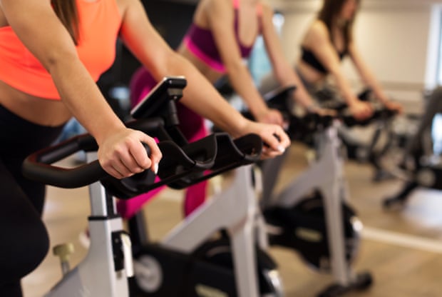 A group of women train on exercise bikes in a gym.