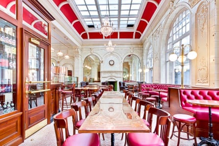 The interior of a pub with red leather chairs, high windows, a glass ceiling and Edwardian lamps.