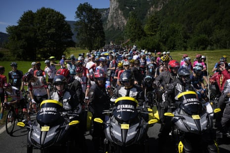 Riders in the pack wait behind organisation motorbikes after the race was stopped due to protestors blocking the route.