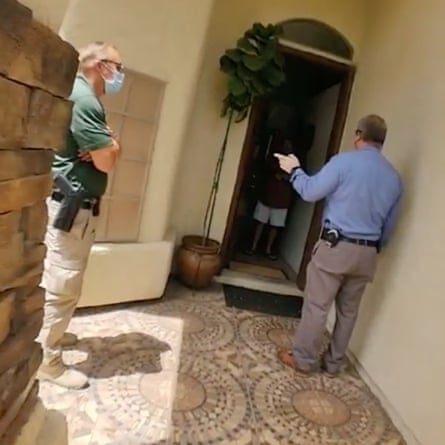 Two officers wearing civilian clothing and sidearms stand near the front entrance of Guillermina Fuentes’ home. An unidentified person stands inside the doorway.