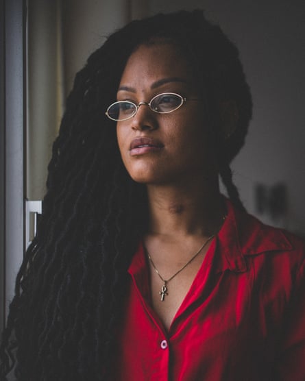 Portrait of Naira Santa Rita wearing a red shirt and glasses.