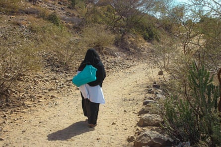 A woman in a black burqa walks along a desert path carrying a bag