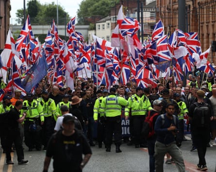 Large crowd of people waving union flags as a line of police officers stand in front of them