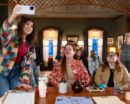 A girl with long dark curly hair taking a selfie with others holding spoons on their noses