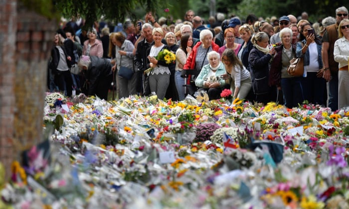Crowds gathered outside Sandringham House. In the foreground, hundreds of bunches of flowers lie on the floor. 