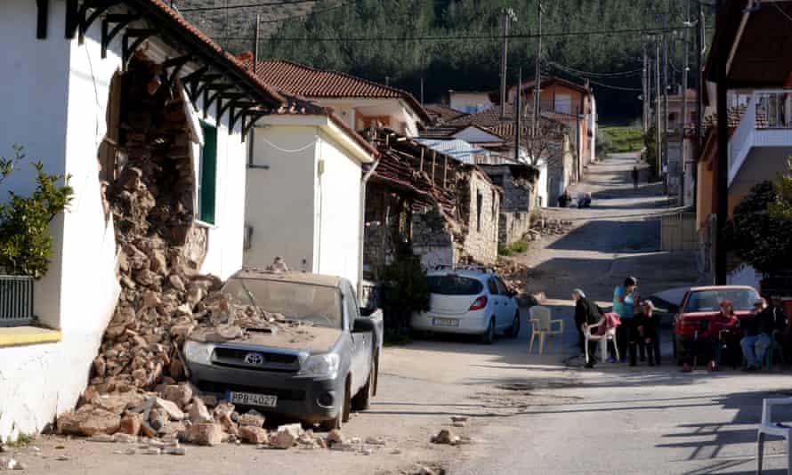 People sit outside damaged homes in Damasi