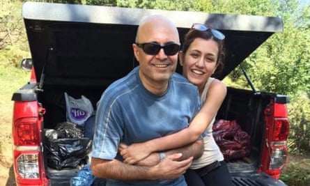 A smiling man is hugged from behind by a young woman.