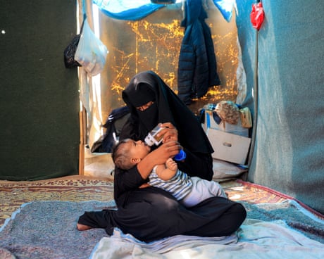 A woman feeds her child with a bottle in a tent