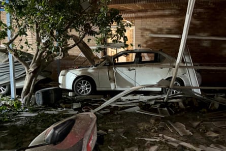 A damaged white saloon car is surrounded by debris that has fallen from the buildings around it.