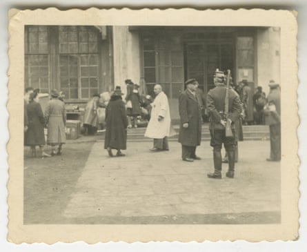 Mientras los residentes judíos se reúnen en Breslau, un policía alemán con un rifle oculta parcialmente al jefe de operaciones de la Gestapo detrás de él.