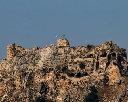 View from below of the stone structure on a hilltop flying the two flags