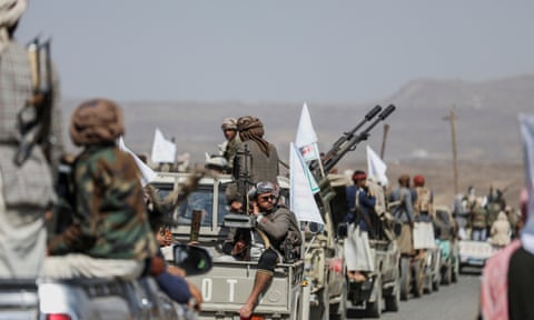 A line of military vehicles lined with men wearing khaki uniforms and bearing weapons.