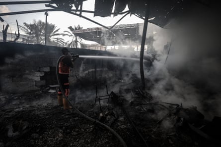 A firefighter hoses charred wreckage of a warehouse