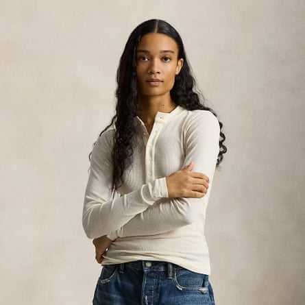 A model wears a cream rib-knit Cotton Henley Shirt by Polo Ralph Lauren. The model also wears dark blue jeans and has long dark hair and their arms folded across the chest.