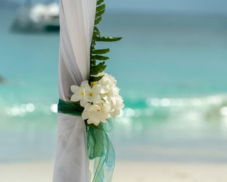 A white flower tied with green ribbon to a post, with the sea behind it