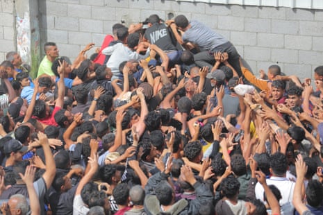 Palestinians reach out for bread being distributed through a bakery window in Nusseirat refugee camp after limited flour supplies entered the Gaza Strip on Thursday