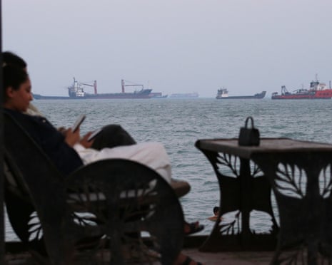Residents check their phones as they sit at a cafe overlooking commercial vessels anchored in the strait of Hormuz off Bandar Abbas in Iran on Sunday