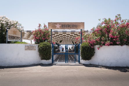The gated entrance to a private beach, with white-washed walls and bushes of pink and white flowers and