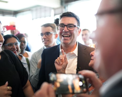 Andy Burnham surrounded by supporters, one of whom is taking a photo using a phone