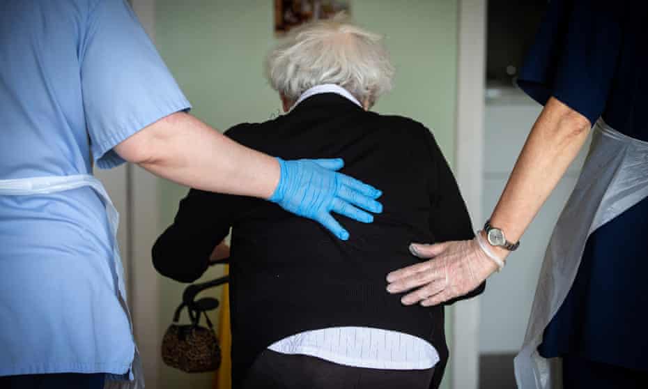 Care workers help an older person to walk in a care home