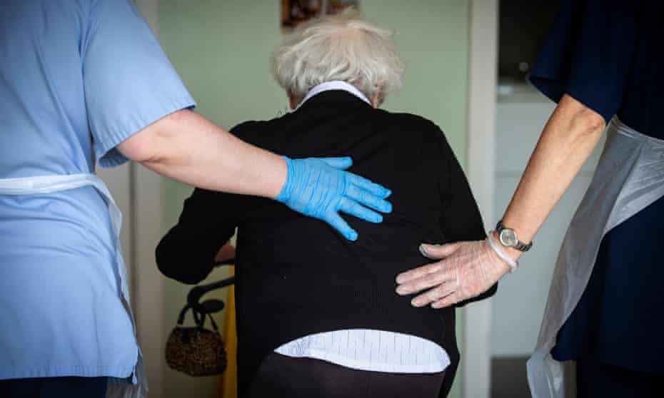 carers wiith hands on back of elderly lady with walker
