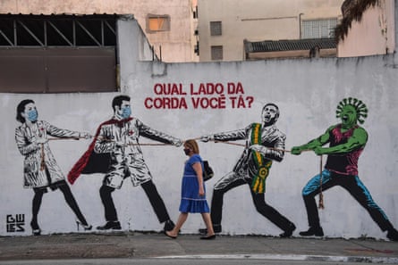 A mural on a wall depicting Jair Bolsonaro and a green, virus-like figure representing Covid-19 pulling a rope against health workers