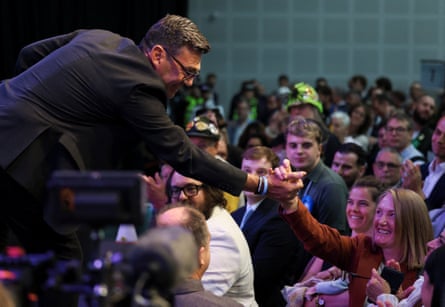 Andy Burnham reaching down from a stage to shake hands with a woman in a crowd of people