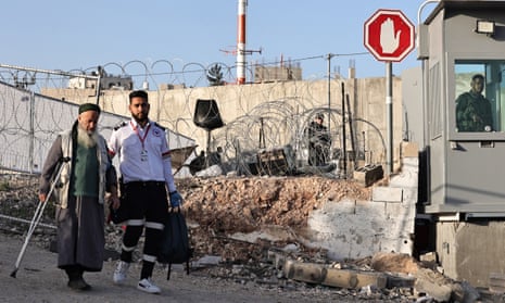 A soldier looks on as an elderly Palestinian man is helped to cross an Israeli checkpoint in Qalandia in the occupied West Bank