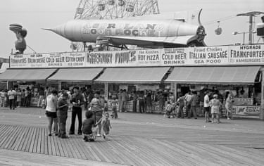 People stand on a boardwalk in front of a restaurant with a model of a rocket ship on the rooftop.