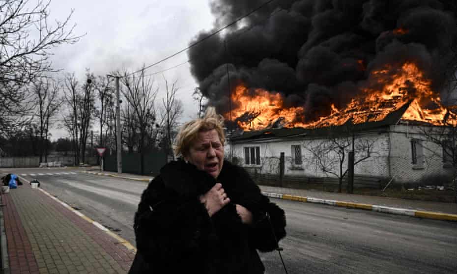 A woman stands in front of a house burning after being shelled in the city of Irpin, outside Kyiv, on 4 March 2022.