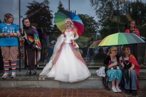 People in costume gather, some holding Pride flag umbrellas