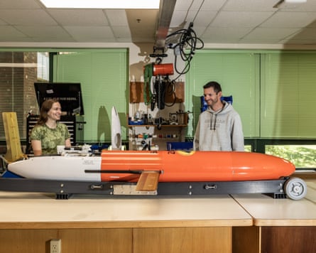 A young woman and a young man in a lab with a large torpedo-shaped instrument