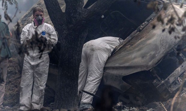 people in white suits and masks stand by vehicle, one bends into vehicle