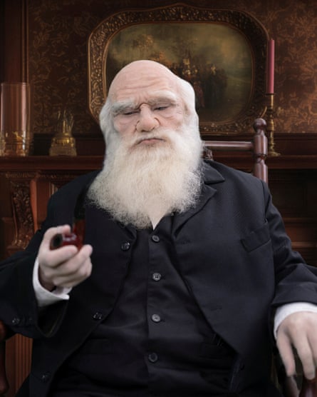 A person in a black suit with prosthetic make-up and a false beard poses as Charles Darwin
