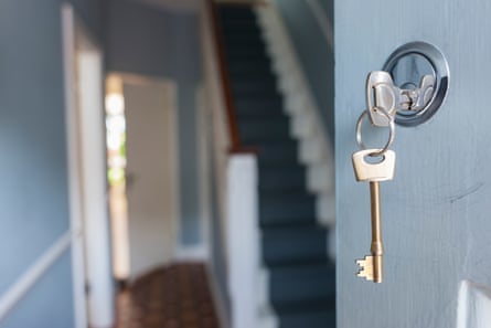 Closeup of keys in lock of front door of house; one key is in the lock and the other on the ring is hanging down