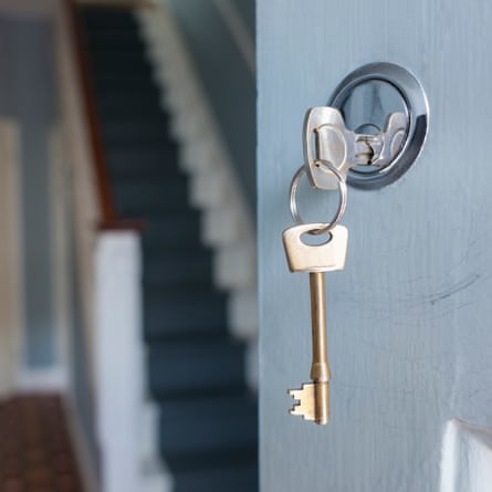 Closeup of keys in lock of front door of house; one key is in the lock and the other on the ring is hanging down