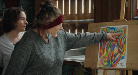 film still of a woman pointing at a painted picture on a board