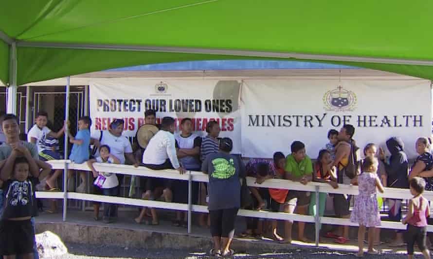Children with their parents wait in line to get vaccinated outside a health clinic in Apia, Samoa after the government declared a state of emergency and mandated that everybody get vaccinated.