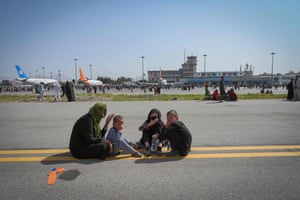 People sit along the tarmac as they wait to leave the airport