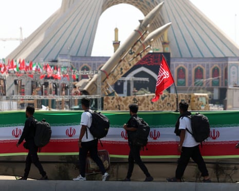 A line of four young people walk past Iranian missiles on display in Tehran's Azadi Square
