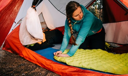 A female camper deflates an inflatable mattress inside a tent