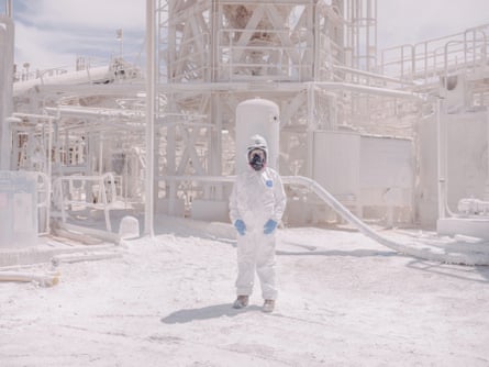 A worker in a mask, goggles and protective overalls in a chemical plant where every surface is covered in white dust
