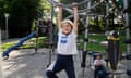 A 10-year-old girl hangs from the bars in a playground while her eight-year-old brother sits on the equipment behind her.