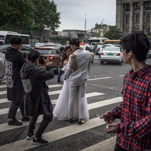 People pass a couple posing for their pre-wedding photos on a road in Wuhan