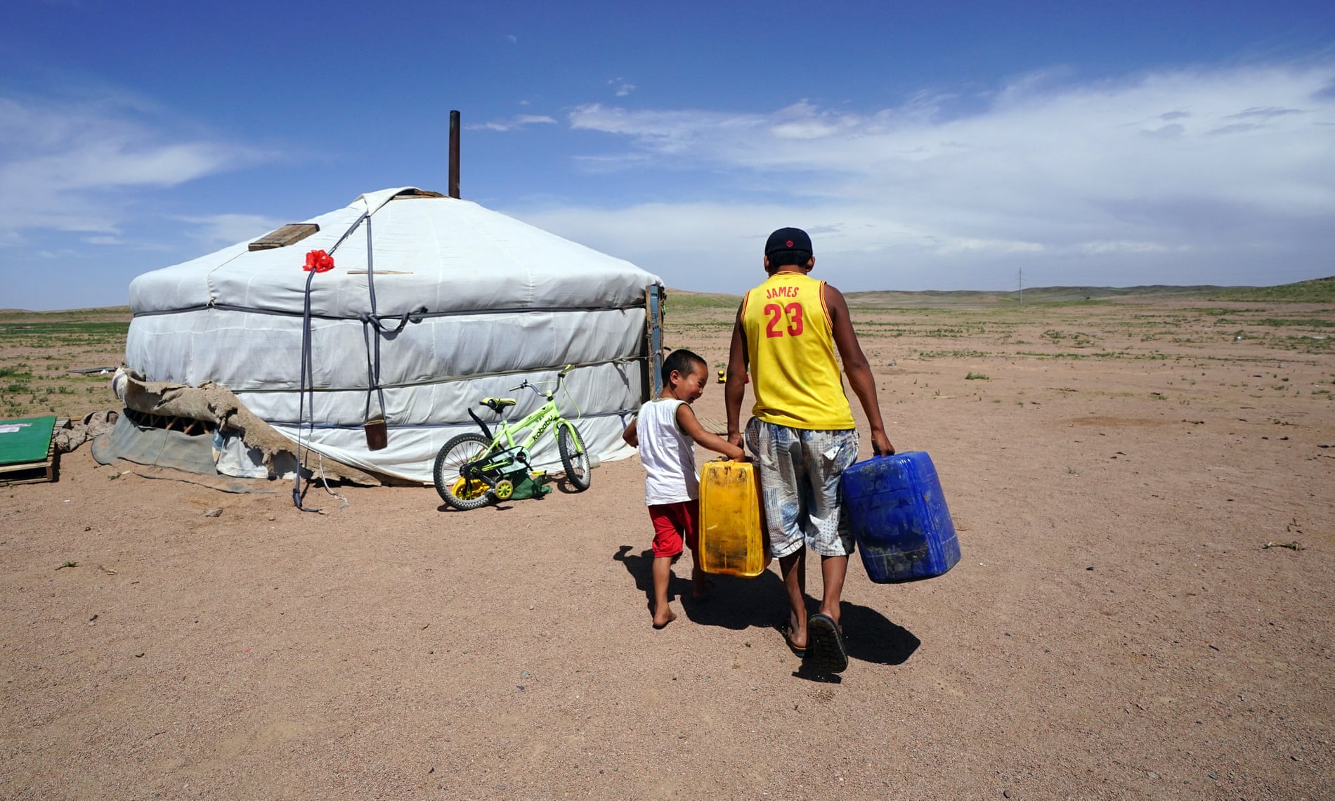 Orgilbayar and his little brother Munkhbat carry water to their father’s ger in Khanbogd Sum, southern Gobi, Mongolia. The Oyu Tolgoi mine is visible in the background