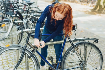 Young redhead woman chaining her bicycle to a metal rack in town with a padlock and chain