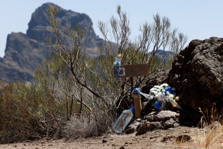 white flowers, tied with blue ribbon, have been placed on a dry, rocky hillside by a small sign bearing his photo and a message.
