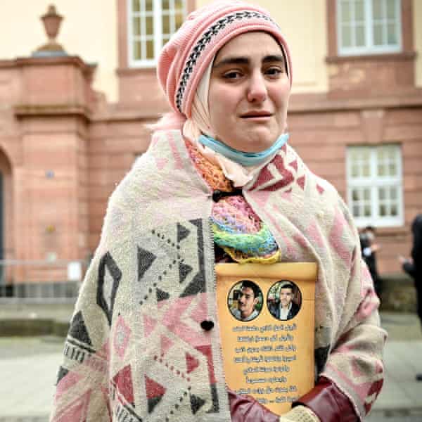 A tearful woman in a shawl and headscarf  holds photos of two men with Arabic script underneath