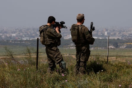 Two Israeli soldiers with weapons stand on the Israeli side of the Israel-Gaza border looking into the Palestinian territory